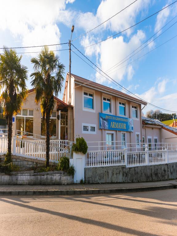 Fachada de la residencia Armayor con dos residentes sentados en la terraza tomando el sol.
